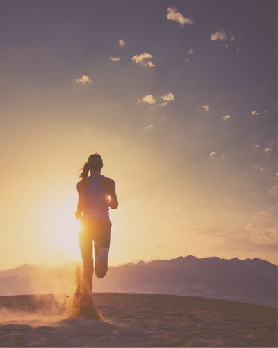 Runner running on sand with sun rising and light beaming